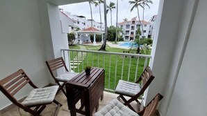 Ein Balkon mit Tisch und Stühlen, mit Blick auf einen Pool und Grünflächen.