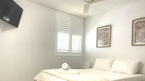 Ein Schlafzimmer mit einem Bett, einem Deckenventilator, einem Fenster mit Jalousien und zwei gerahmten Bildern an der Wand.