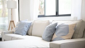 Ein modernes Wohnzimmer mit einem beigen Sofa, hellblauen Kissen und einer Stehlampe.