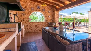 A stone-walled outdoor kitchen area with a grill, dining table, and wicker furniture. - Villa Sanchez (Campos)