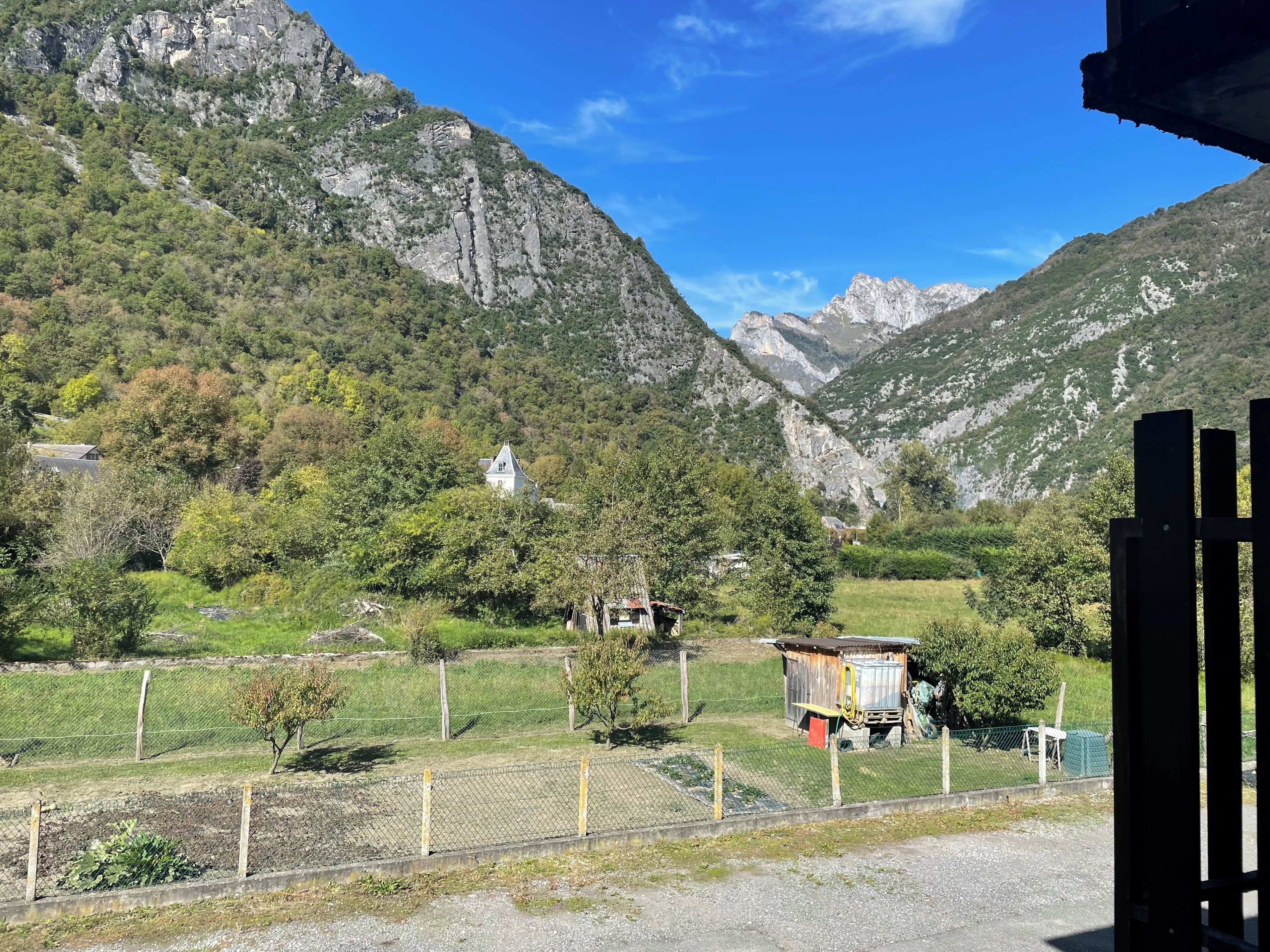A mountainous landscape with a white building surrounded by greenery and a fenced area.