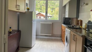 Eine kompakte Küche mit integrierter Waschmaschine und Trockner, einem Kühlschrank und einem Fenster mit Blick auf ein Haus und Bäume.