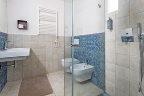Une salle de bain avec une douche à parois de verre, un lavabo blanc, un bidet et des toilettes.