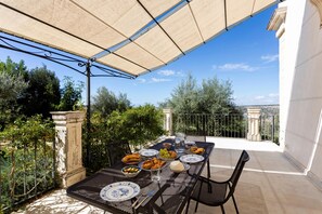 An outdoor dining area with a table set for a meal, surrounded by greenery and a clear sky.