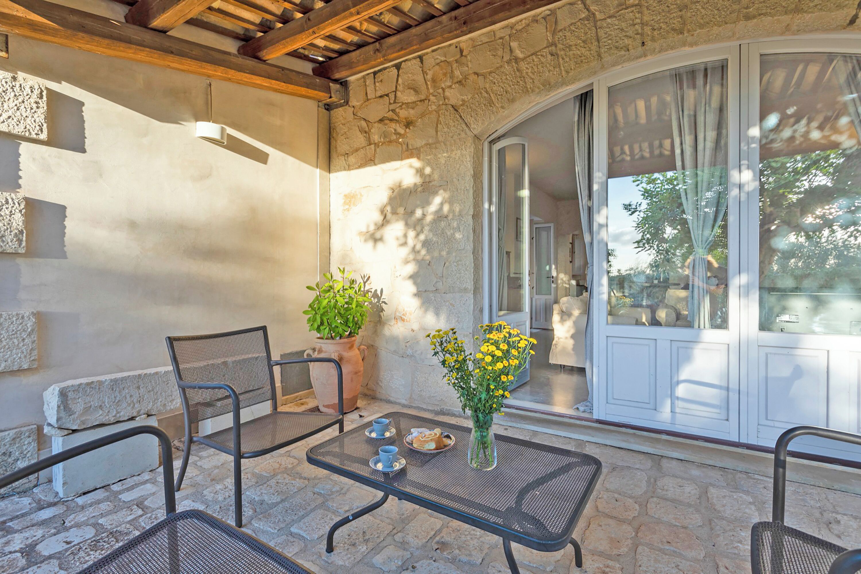 A stone patio with outdoor furniture, a potted plant, and a vase with yellow flowers.