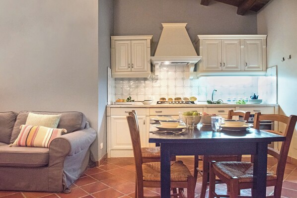 Une cuisine avec des meubles blancs, une table à manger et un canapé avec un coussin.
