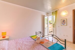 A bedroom with a bed, a nightstand with a lamp, a window with curtains, and a door leading outside. - Casa Lory 1 Cosy near the Sea, Nardò, Italy (Nardò)