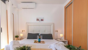 A hotel room with a large bed, two bedside tables, a wall-mounted air conditioner, and a wooden door.
