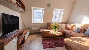 A living room with a flat-screen TV, wooden entertainment unit, brown sofa, and a red patterned rug. - Cozy Bovec Apartment in Soča Valley, Bovec, Slovenia (Bovec)