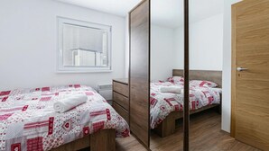 A bedroom with two beds, a mirror, a window, and a wooden door. - Cozy Bovec Apartment in Soča Valley, Bovec, Slovenia (Bovec)