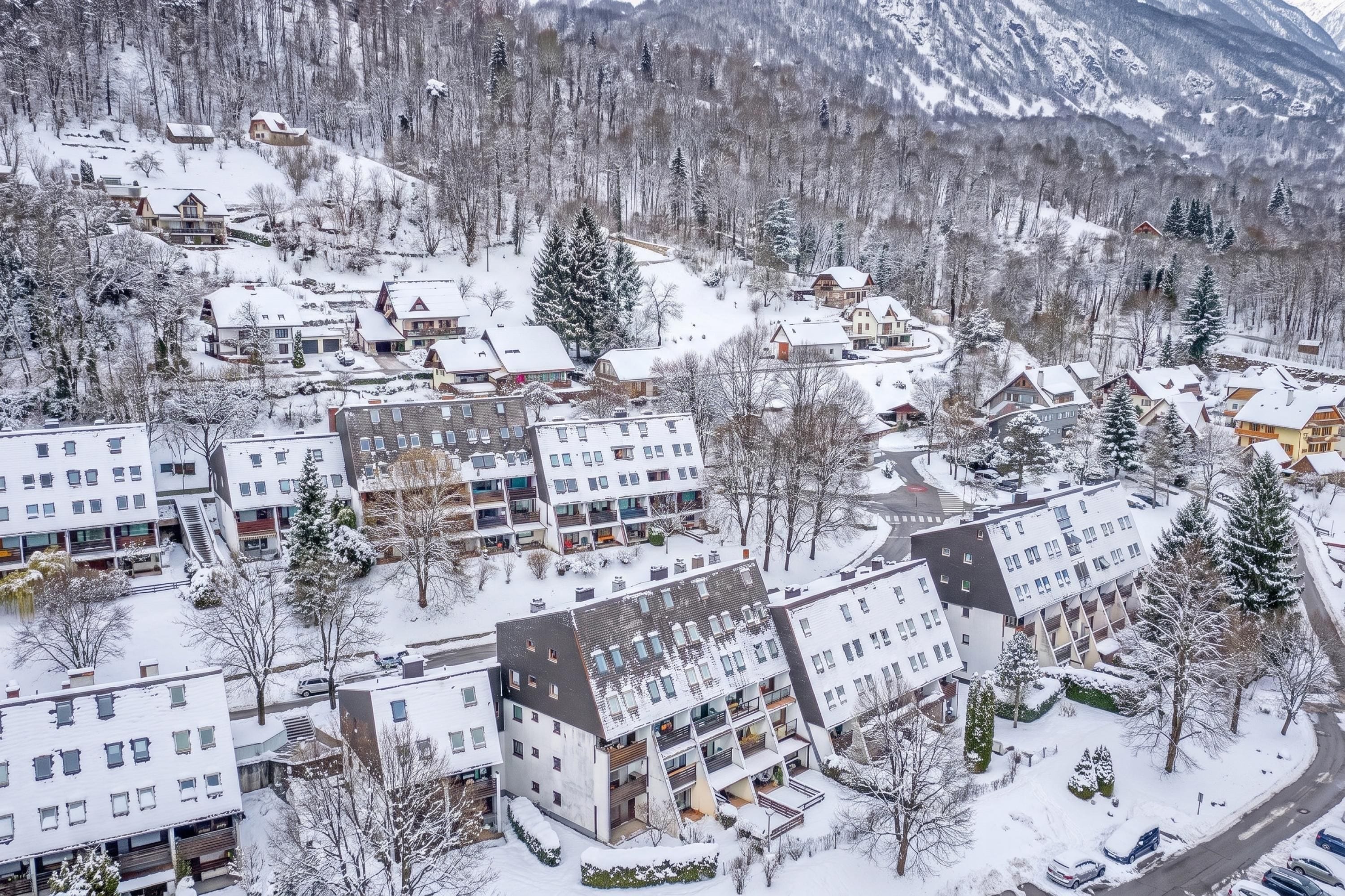 A residential area with multiple apartment buildings, surrounded by snow-covered trees and mountains.