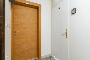 Une porte en bois avec une poignée, une porte blanche avec une poignée et un interphone fixé au mur.