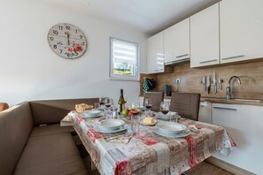 Un comedor con una mesa preparada para cuatro personas, un reloj y una ventana con persianas.