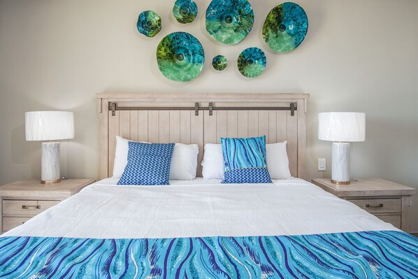 A bedroom with a wooden headboard, two bedside tables with lamps, a bed with white bedding and blue patterned pillows, and a wall with circular decorative plates.