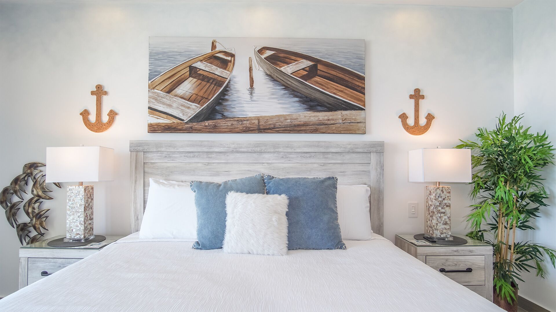Un dormitorio con una cama grande, dos mesitas de noche, un cuadro colgado en la pared con barcos y dos anclas decorativas en la pared.