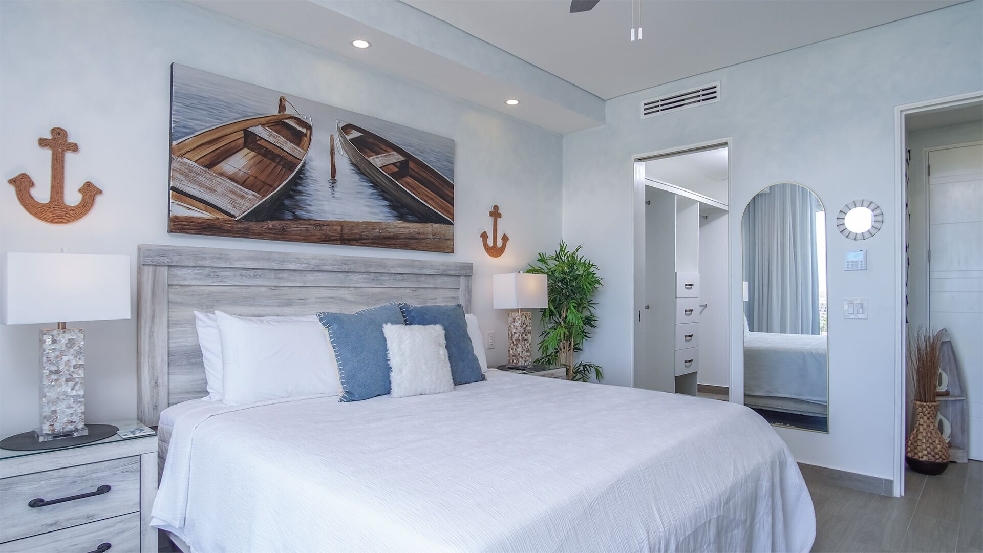 Un dormitorio moderno con una cama grande, un cabecero de madera, un cuadro con barcos y un espejo.