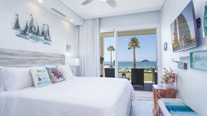 Ein Schlafzimmer mit einem großen Bett, Blick auf den Strand und einem Balkon mit Sitzgelegenheiten.
