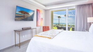 A hotel room with a bed, a table with a towel, a painting of a beach, and a view of the ocean through a glass door.