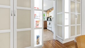 Une cuisine avec des meubles blancs, un plancher en bois et une vue sur la salle à manger.