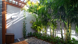Eine Holzterrasse, ein kleiner Garten mit unterschiedlichen Pflanzen und eine Mauer mit einer Tür.