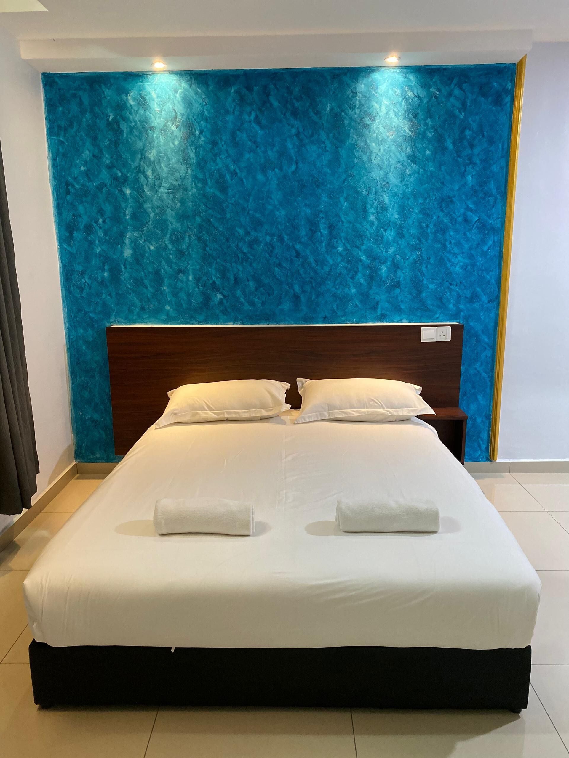 A neatly made bed with white linens and two towels, a wooden headboard, and a blue textured wall behind it.