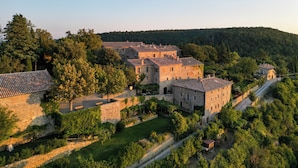 A historic stone building complex with multiple structures, surrounded by lush greenery and a hillside backdrop. - Monteverdi Tuscany (Sarteano)