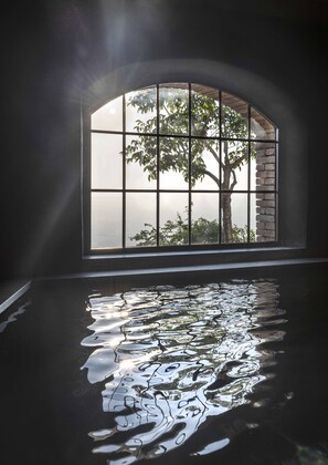 A room with a large arched window overlooking a tree and a body of water. - Monteverdi Tuscany (Sarteano)