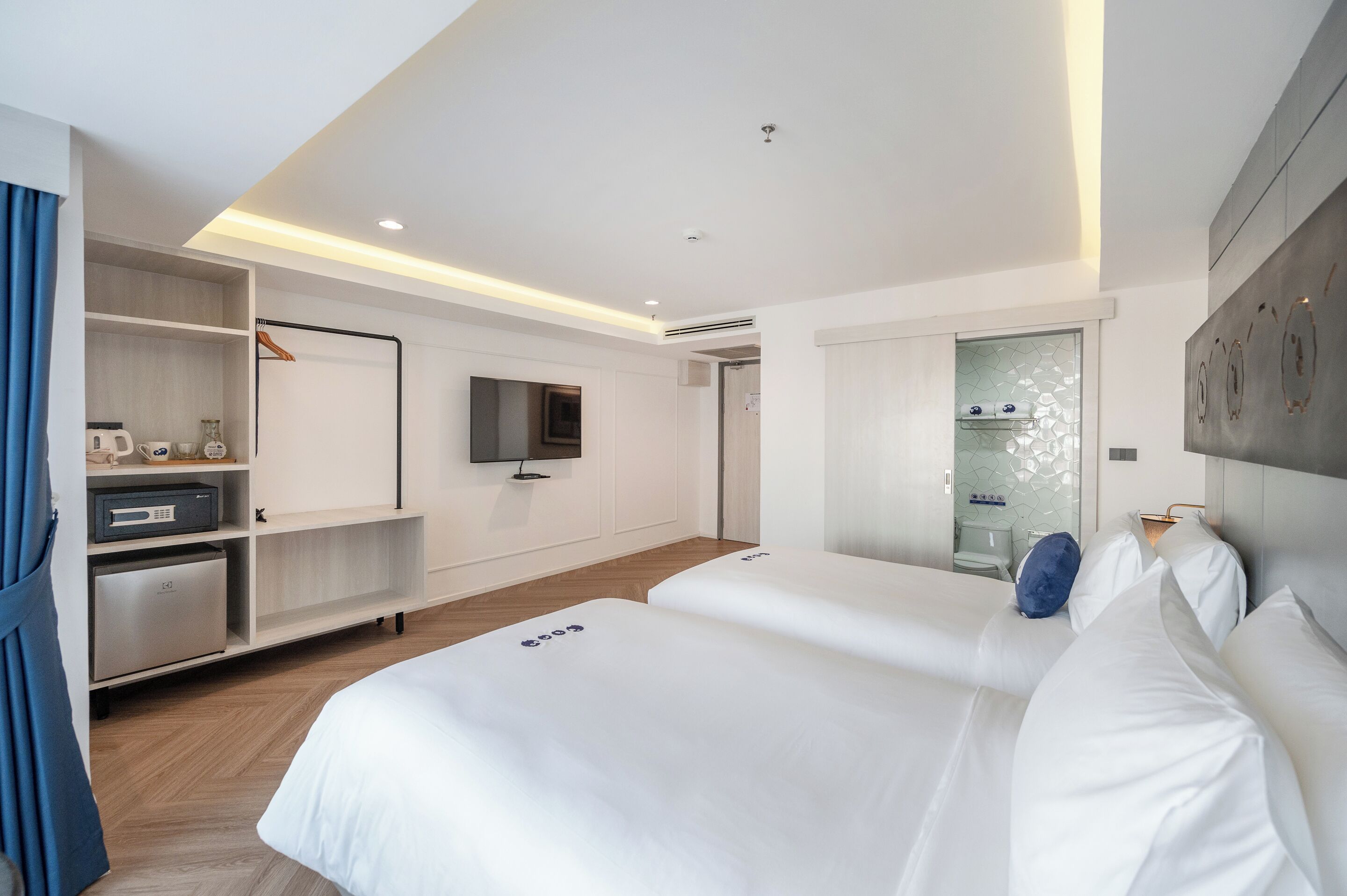 Ein modernes Hotelzimmer mit zwei Betten, einem Flachbildfernseher, einer Minibar und einem Duschbereich.
