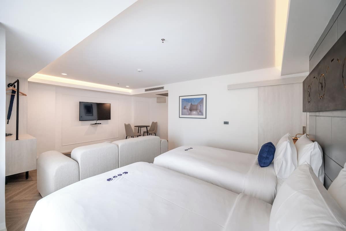 A modern hotel room with a large bed, a TV, a small table, and a seating area.