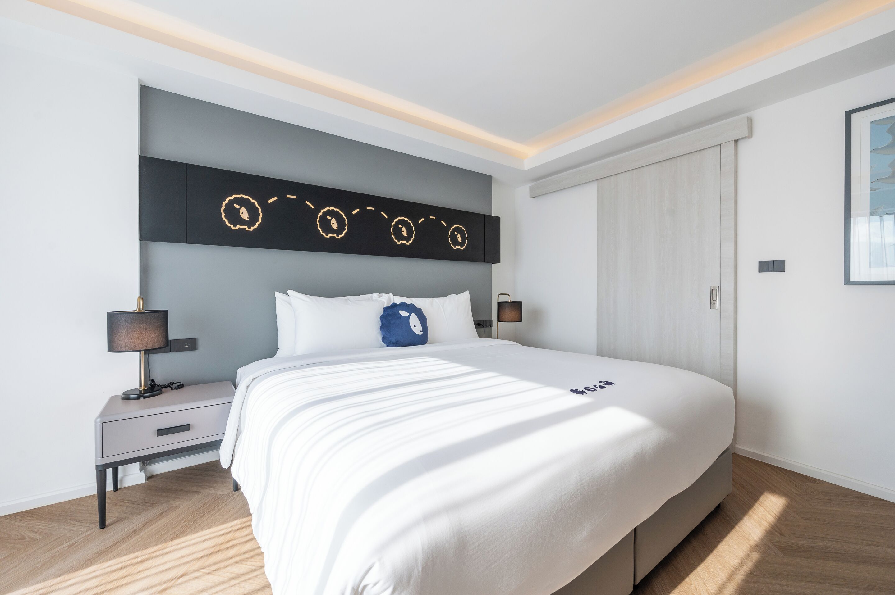 A modern bedroom with a large bed, a bedside table, a nightstand, a wall-mounted light fixture, and a wardrobe.