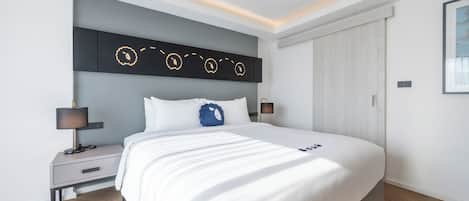A modern bedroom with a large bed, a bedside table, a nightstand, a wall-mounted light fixture, and a wardrobe.