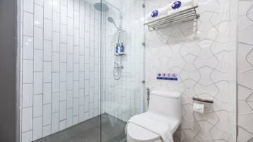 Un baño moderno con paredes de azulejos blancos, ducha con cerramiento de vidrio, inodoro blanco y un perchero con una toalla azul.