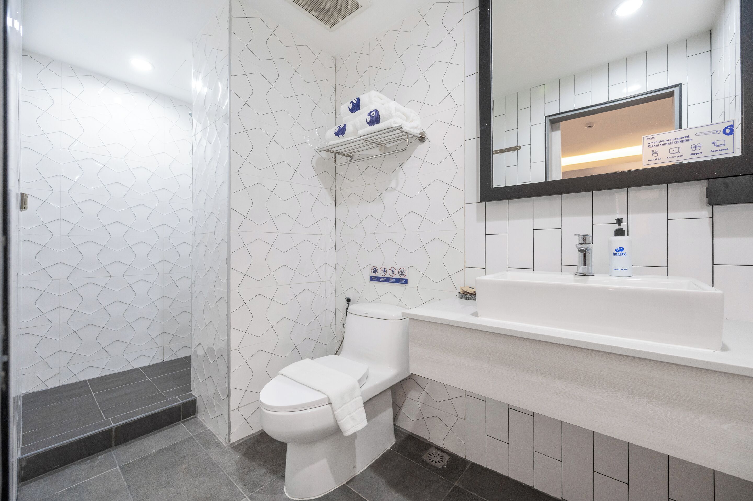 Un baño moderno con inodoro blanco, lavamanos con espejo y zona de ducha.