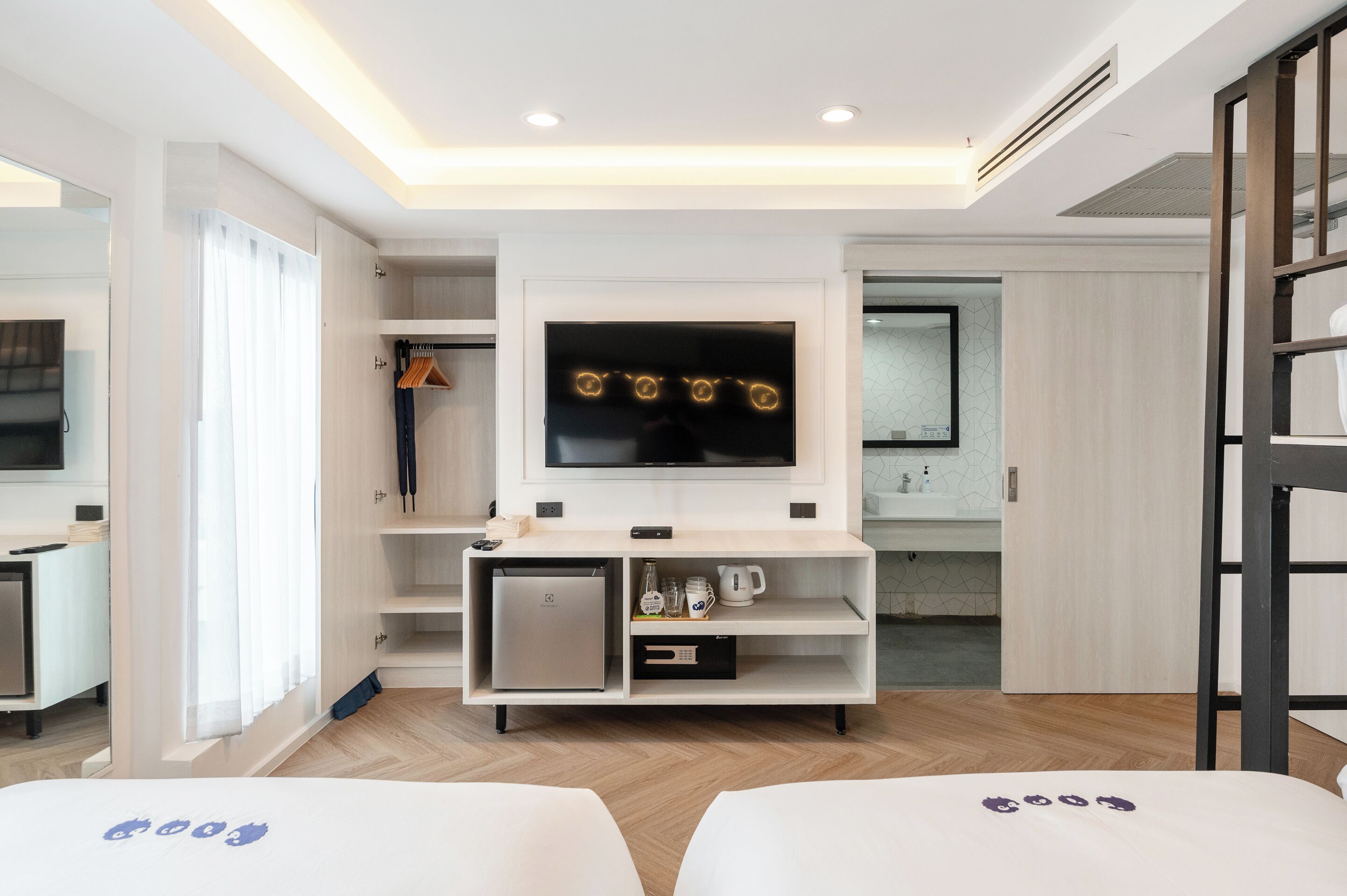 A modern hotel room with a built-in TV, a mini-fridge, a coffee machine, and a small cabinet.