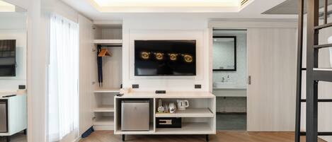 A modern hotel room with a built-in TV, a mini-fridge, a coffee machine, and a small cabinet.