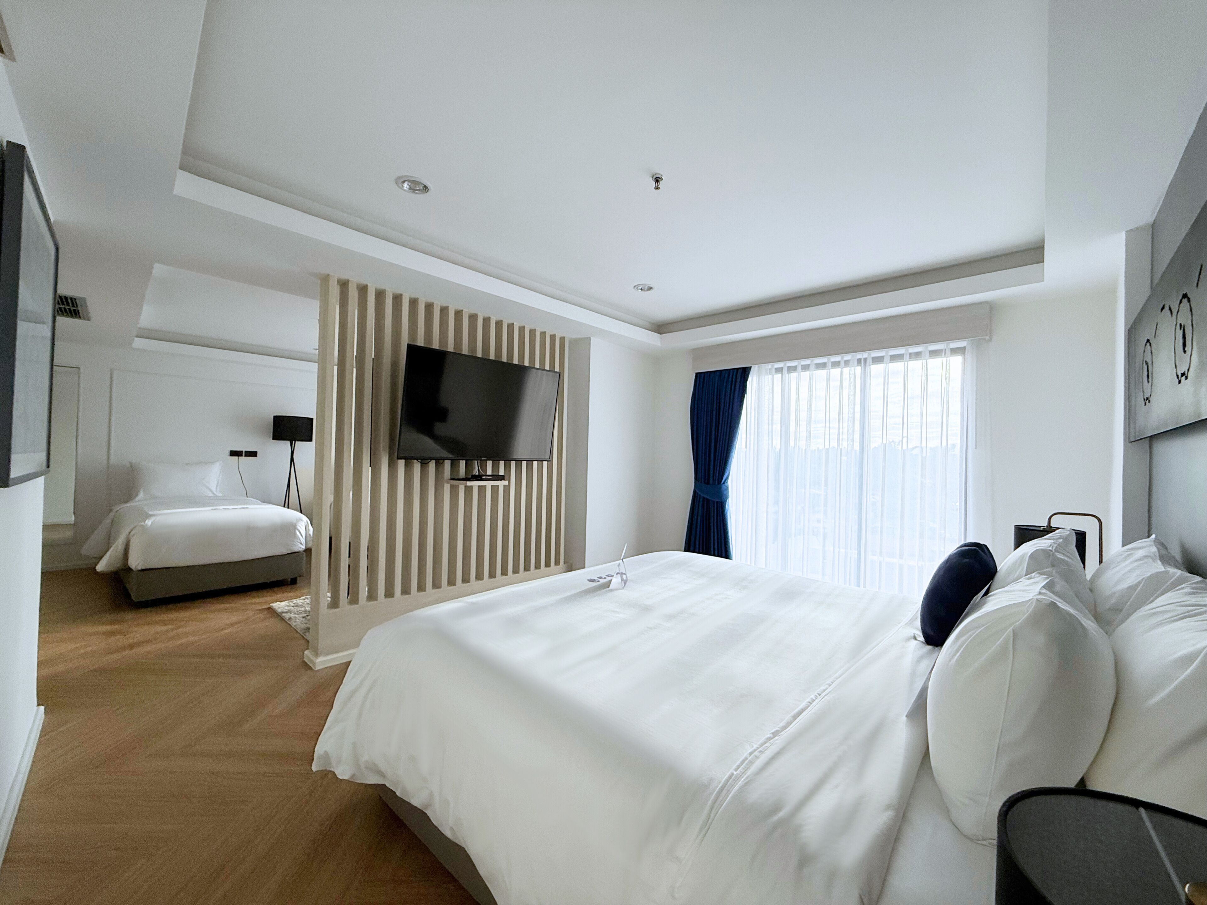 Una habitación de hotel moderna con una cama grande, un televisor de pantalla plana en la pared y una ventana con cortinas.