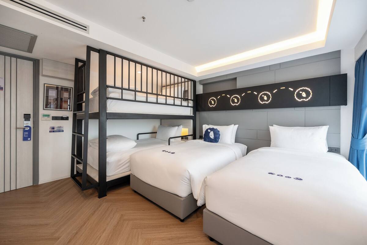 A hotel room with bunk beds, a flat-screen TV mounted on the wall, and a bed with a decorative pillow.
