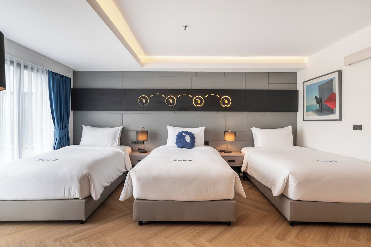 A hotel room with two beds, a modern headboard, bedside lamps, and a framed artwork on the wall.