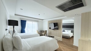 A hotel room with two beds, a TV, a desk, and a separate sleeping area.