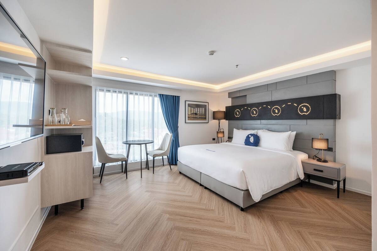 A modern hotel room with a large bed, a desk with a chair, a TV, and a small table.