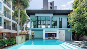A modern hotel with a swimming pool, outdoor seating, and a view of the surrounding buildings.
