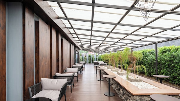 A covered outdoor seating area with wooden walls, stone accents, and a view of greenery.