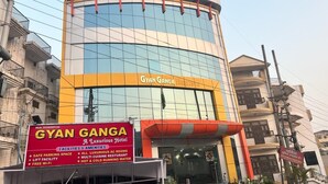 Hotel Gyan Ganga con fachada moderna, amplios ventanales y un cartel que anuncia servicios como estacionamiento seguro, ascensor y Wi-Fi.