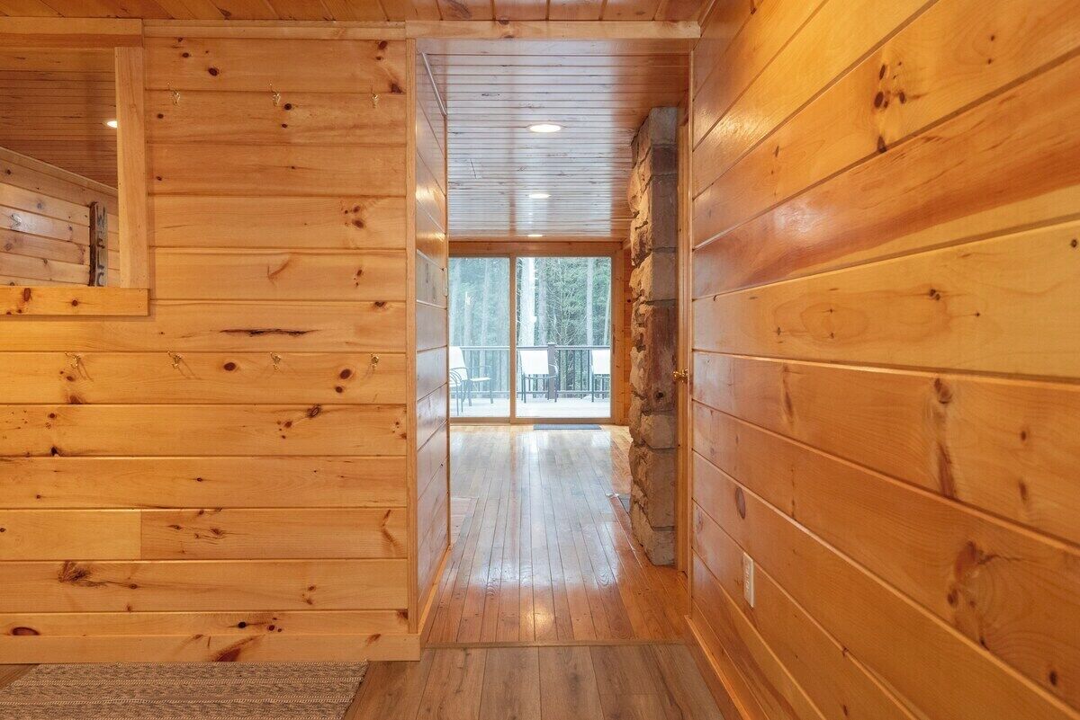 Un couloir intérieur en bois mène à une porte en verre, avec un mur en pierre sur un des côtés.