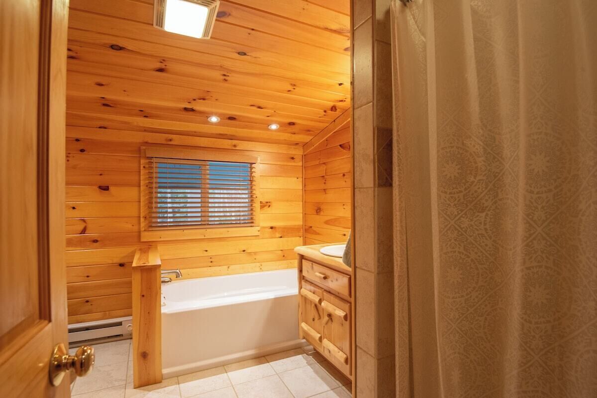 Un baño al estilo cabaña de madera con bañera, muebles de madera y una ventana con persianas.