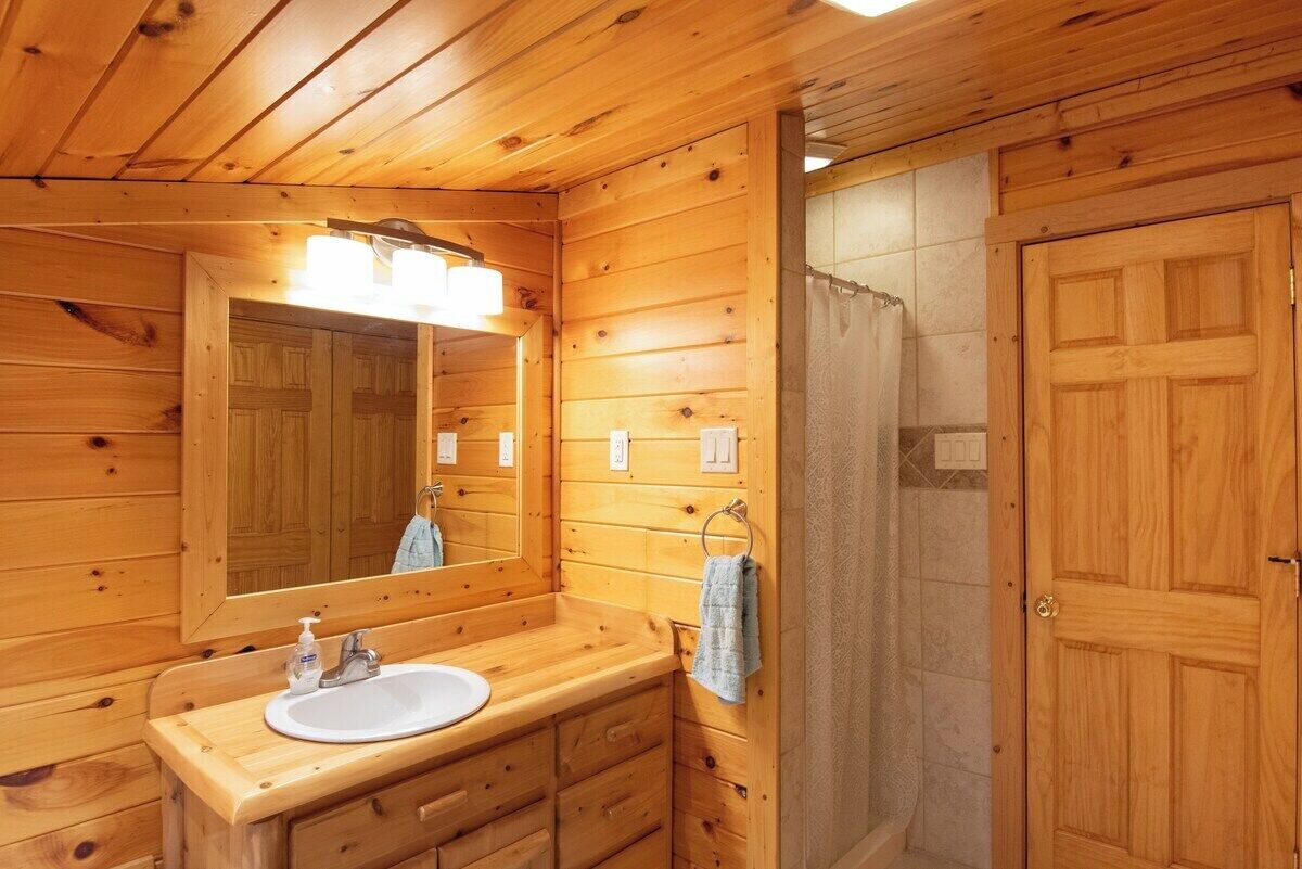Une salle de bain rustique, aménagée dans une cabane en bois, avec un lavabo, un miroir, un porte-serviettes et une douche.