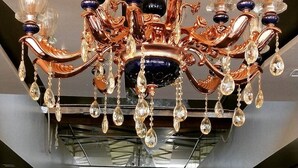 A chandelier with multiple glass and crystal elements, suspended above a sign that reads "THE GRAND KAUSHALYA". - Hotel The Grand Kaushalya (Sohagpur)
