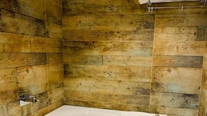 A modern bathroom with a large freestanding bathtub, wooden wall panels, and a glass shower enclosure. - Hotel The Grand Kaushalya (Sohagpur)