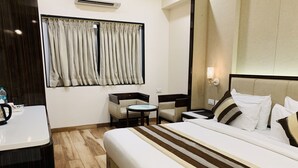 Habitació d'hotel amb un llit gran, una taula petita, una cadira i un escriptori amb una paperera.