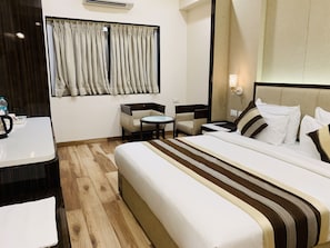 Habitación de hotel con una cama grande, una mesita, una silla y un escritorio con hervidor.